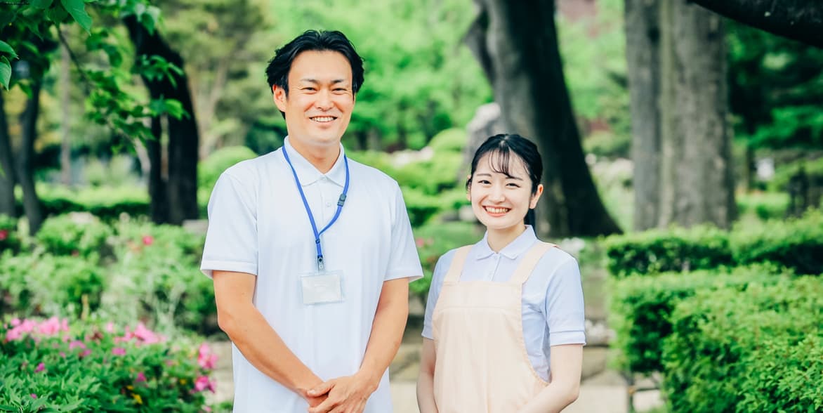 介護施設のスタッフ2名が施設の庭園で笑顔で立っている。